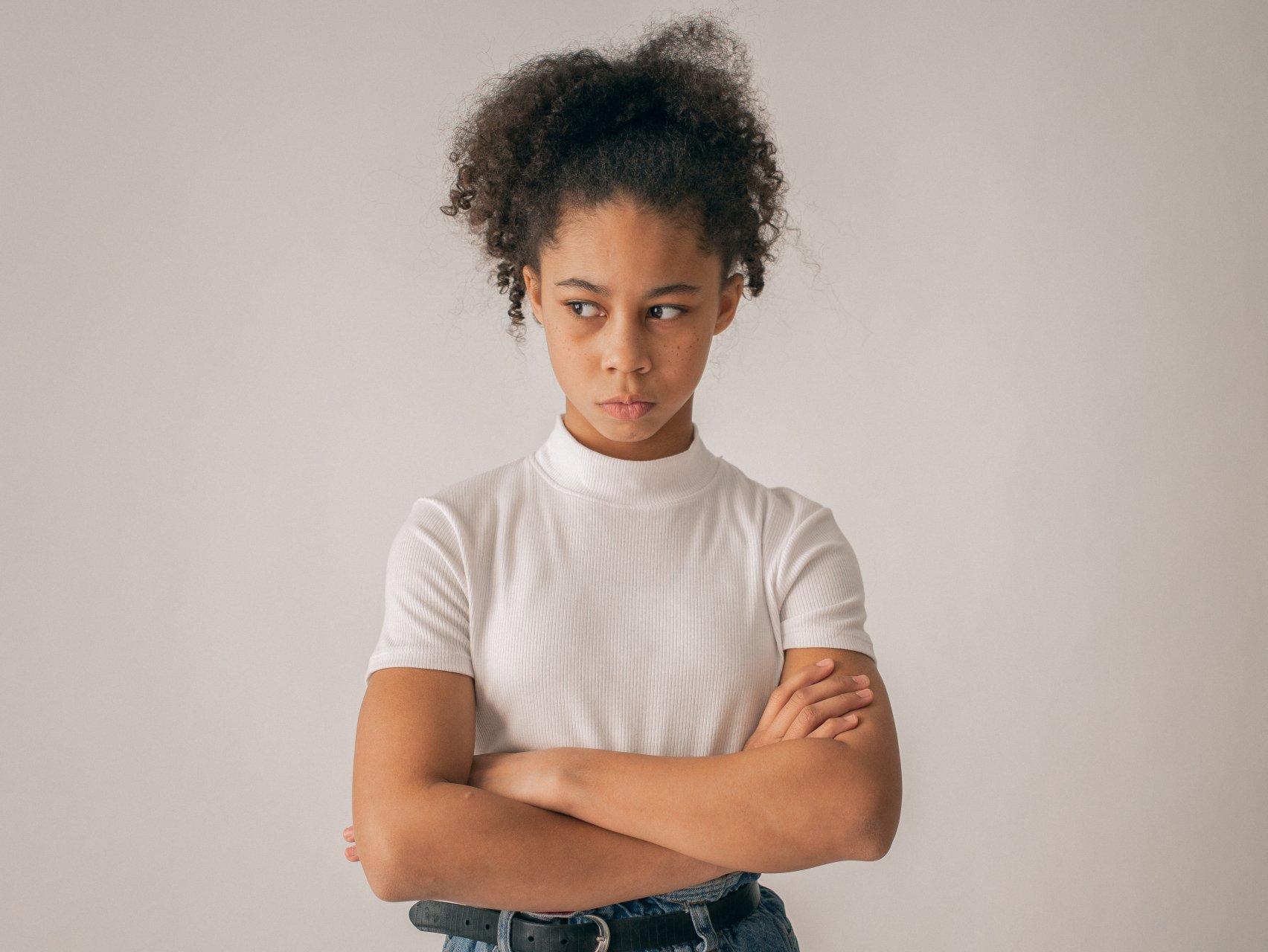 A young girl is standing with her arms crossed and looking at the camera.
