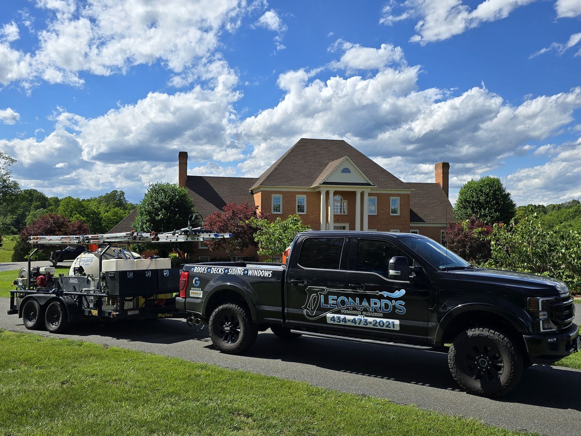 Black truck towing a trailer in front of a large house on a sunny day.