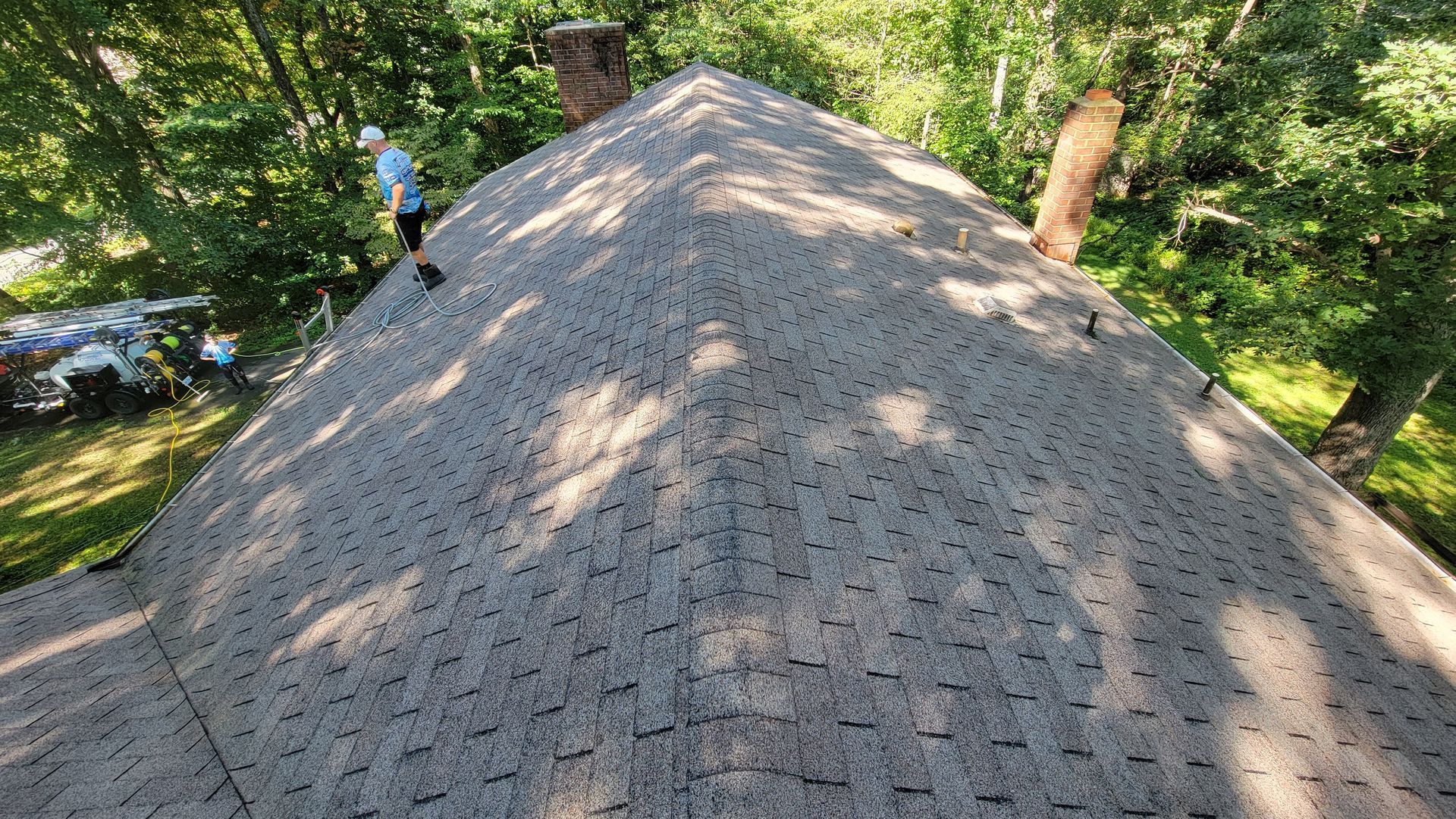 Person on a roof near a chimney; trees in the background; sunlight on brown shingles.