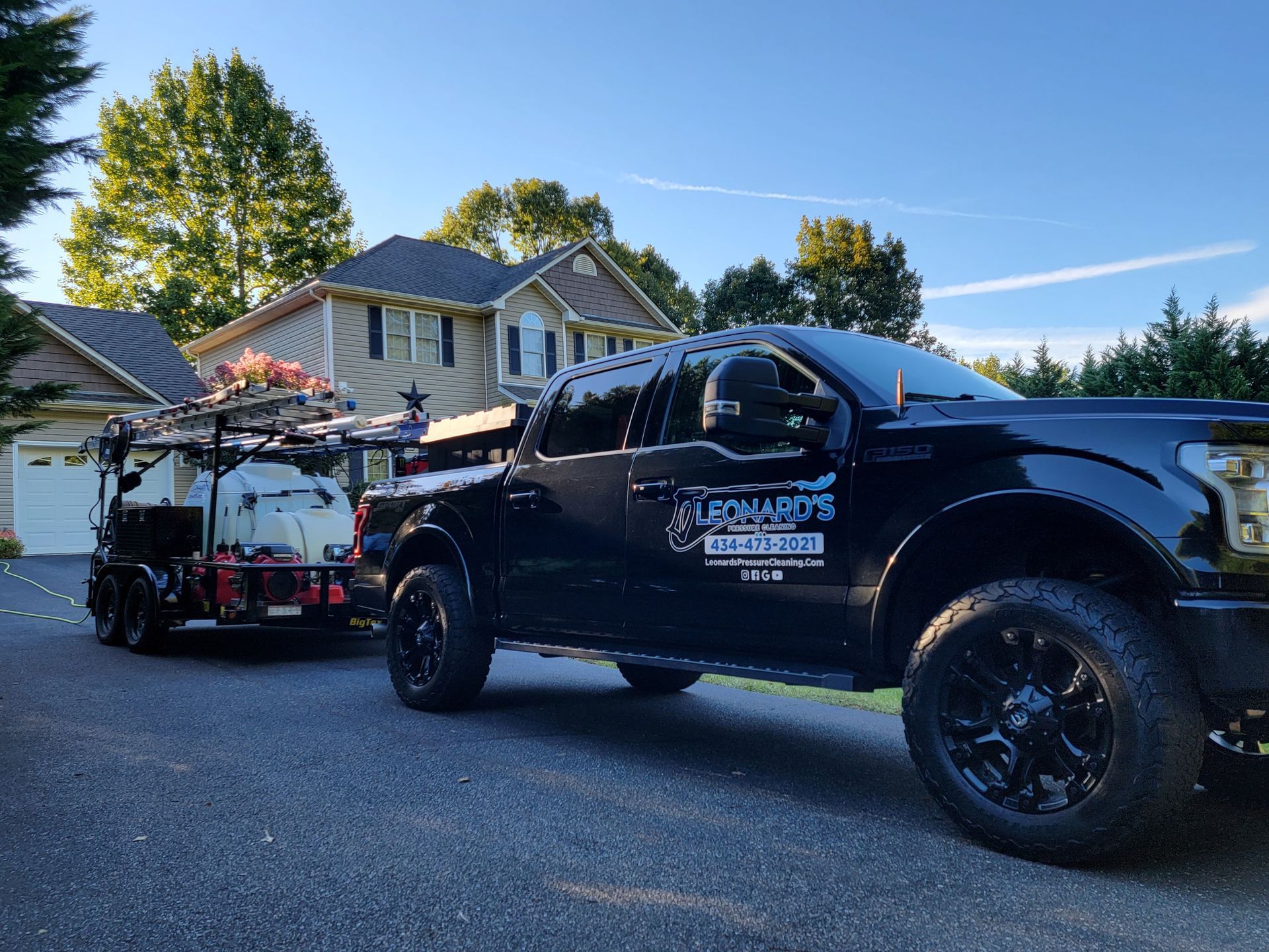 Black truck with trailer, parked in front of a house. Company logo on the truck side.