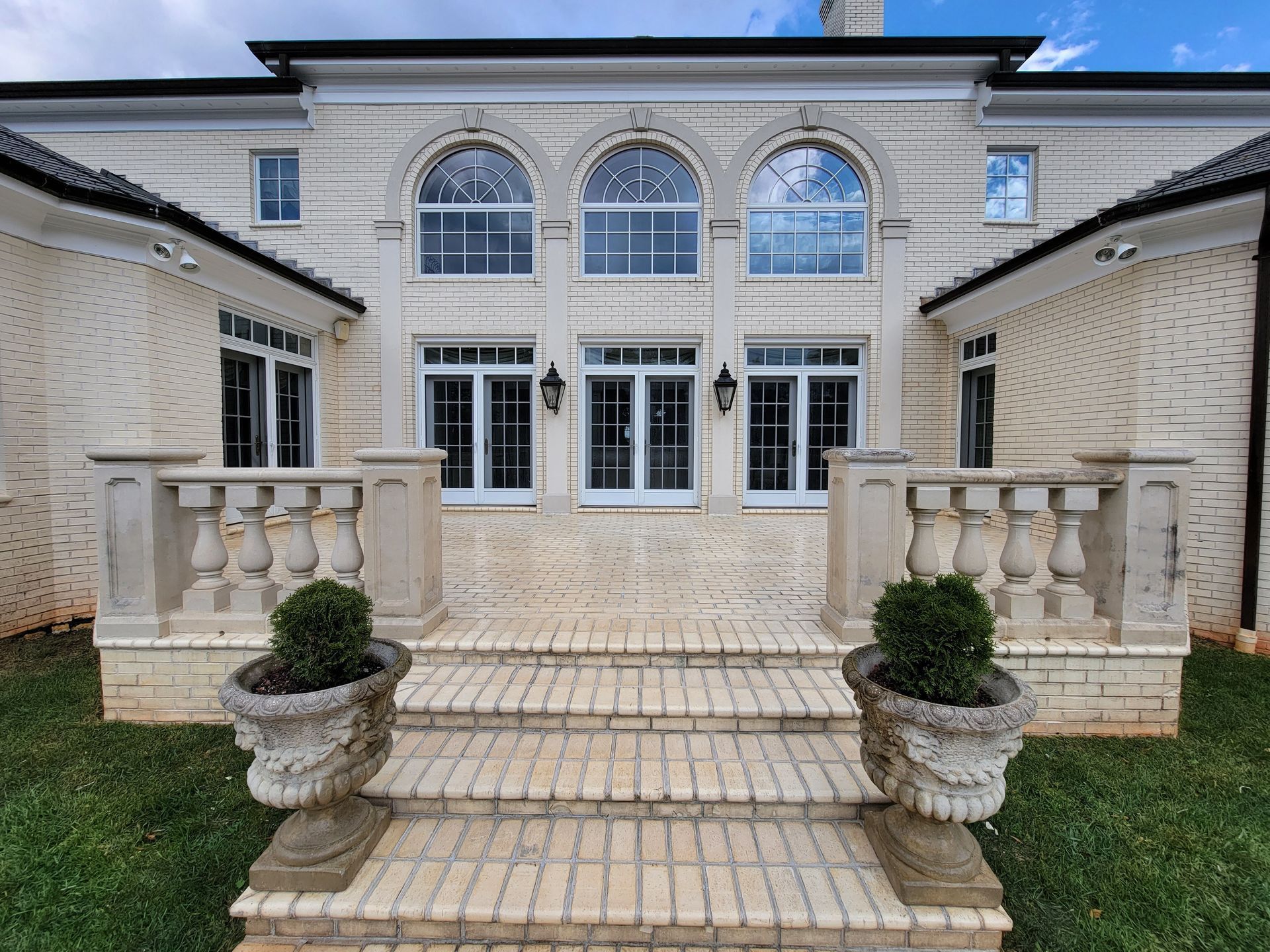 Brick home exterior with arched windows, stone balustrade, brick steps, and urn planters.