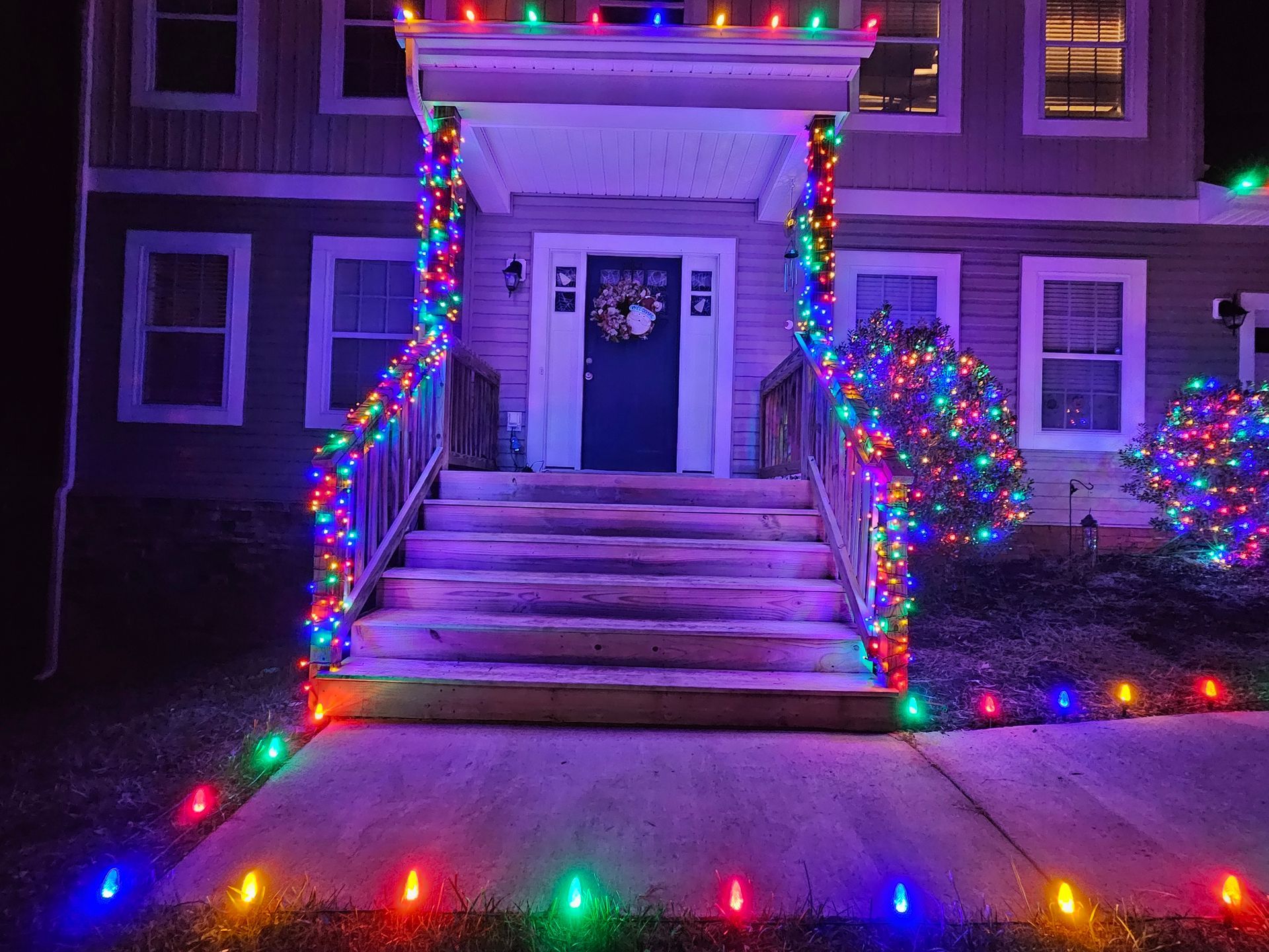 House decorated with colorful Christmas lights on porch and walkway.