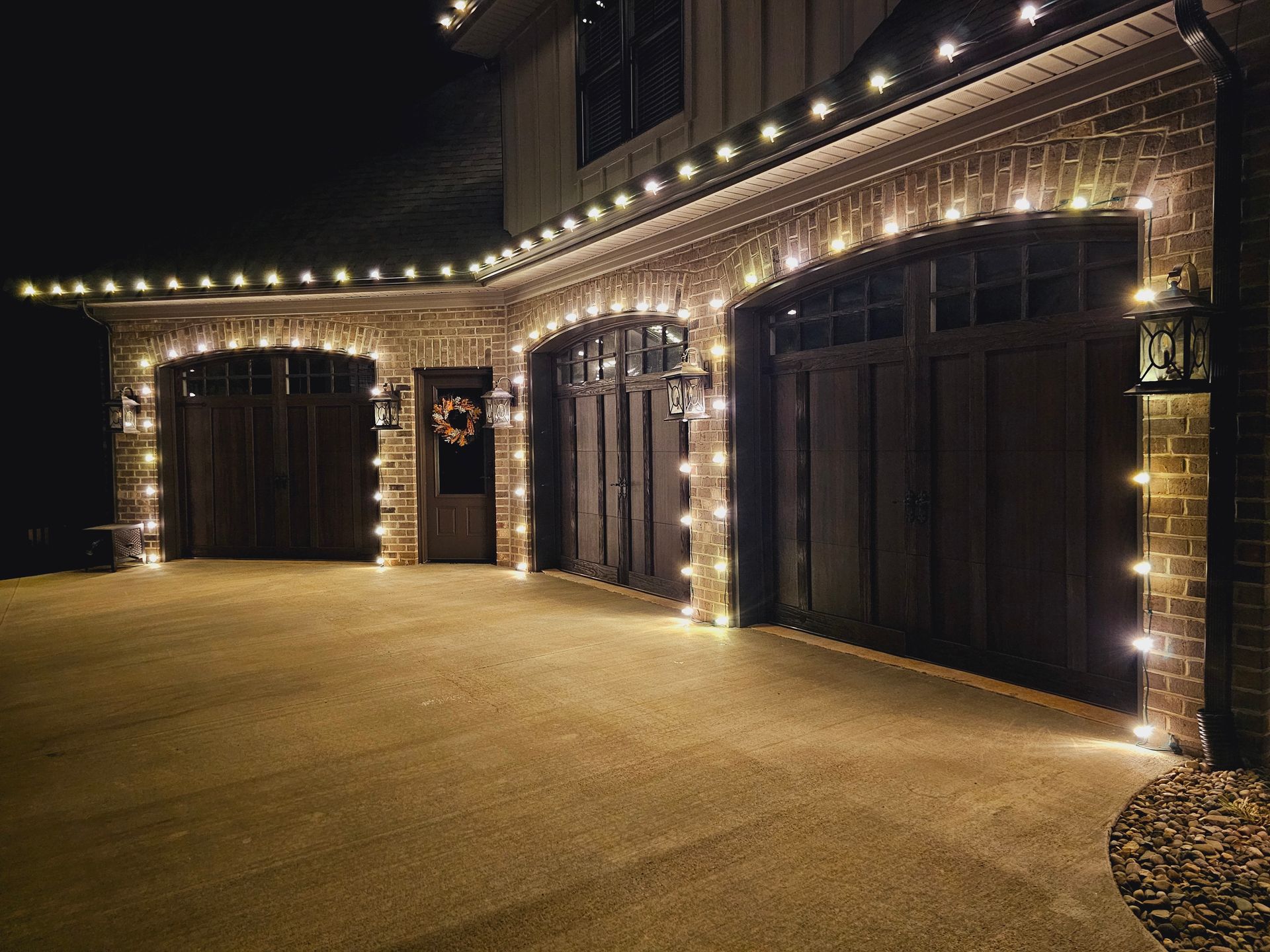 Garage with warm white string lights at night. Brick exterior, dark brown doors.