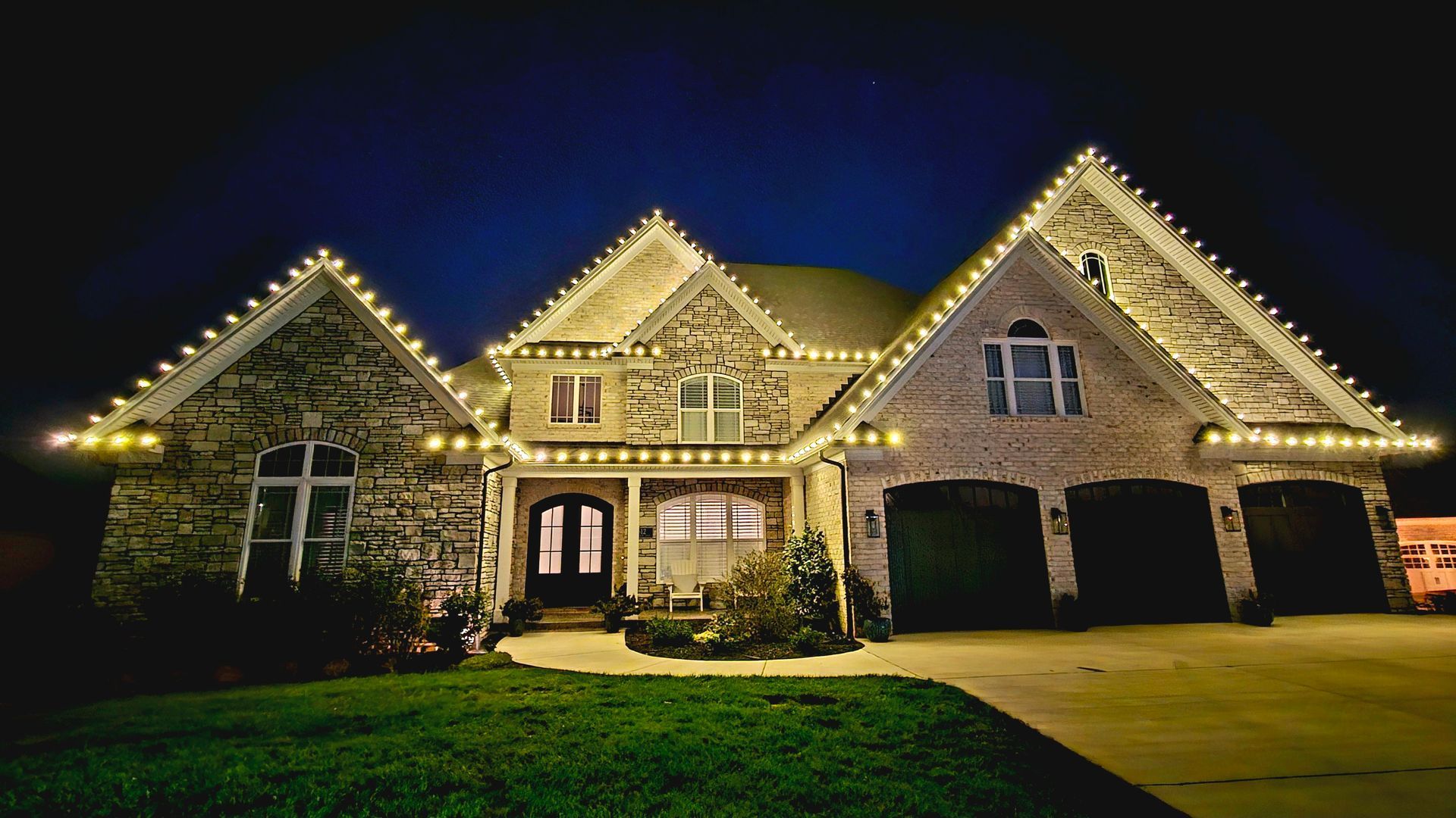 House at night with Christmas lights outlining the roof and window trim.