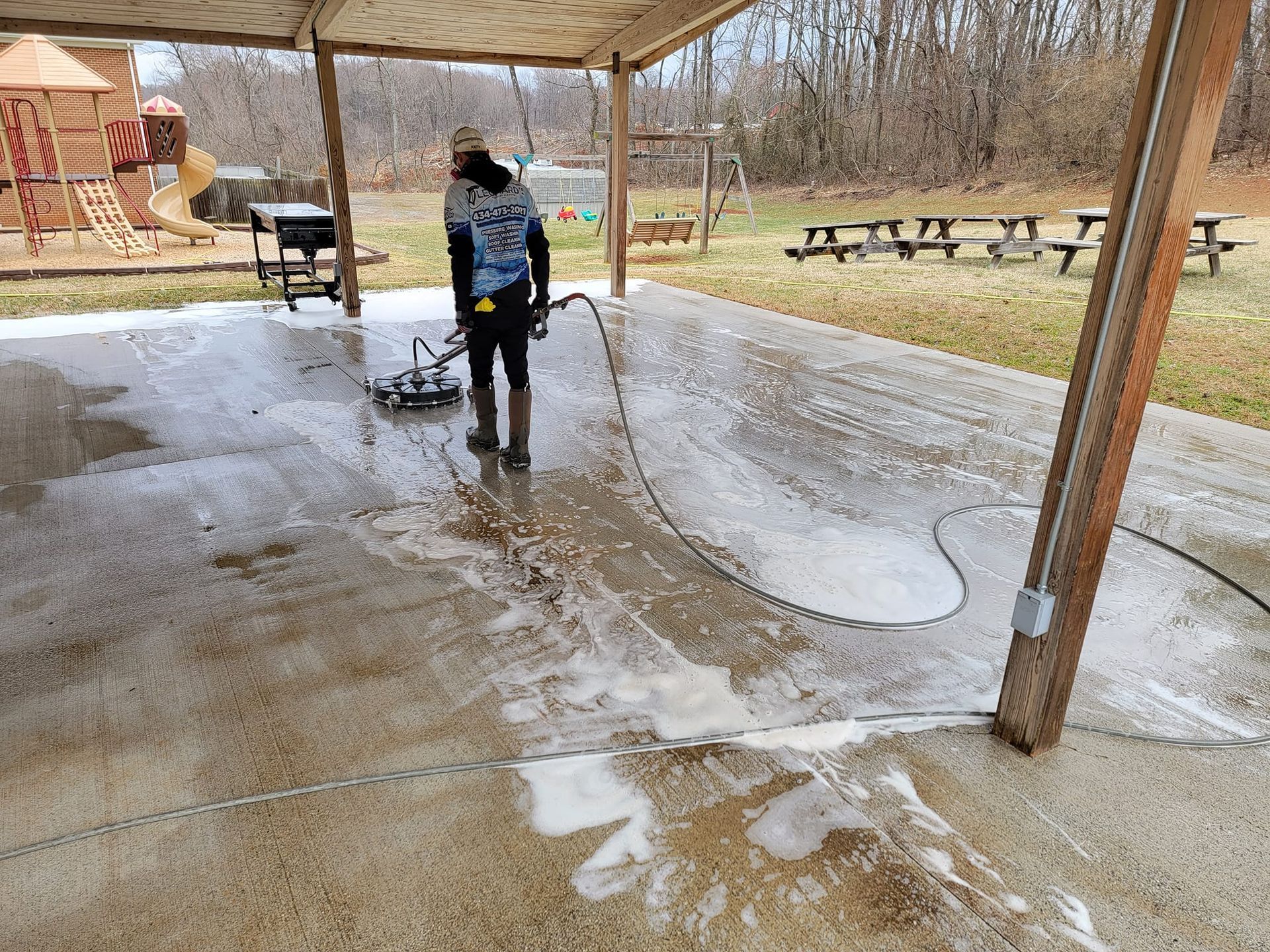 Person power washing a concrete patio under a covered area. Soap suds cover the surface.