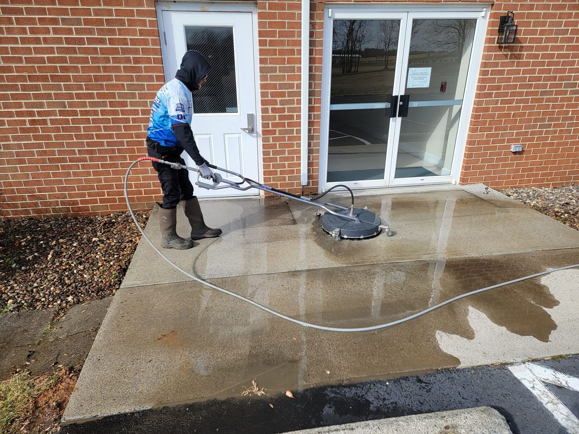 Person power washing a concrete patio outside a brick building.