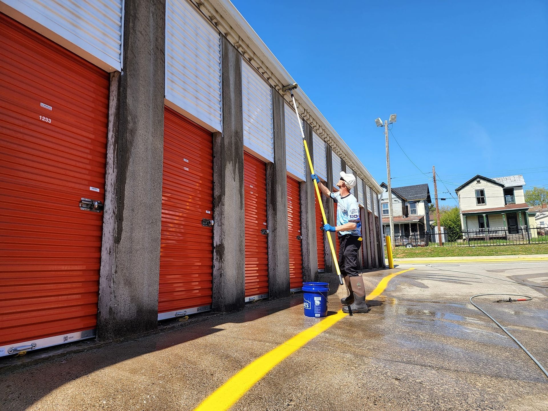 Man power washing exterior of storage units with red doors.