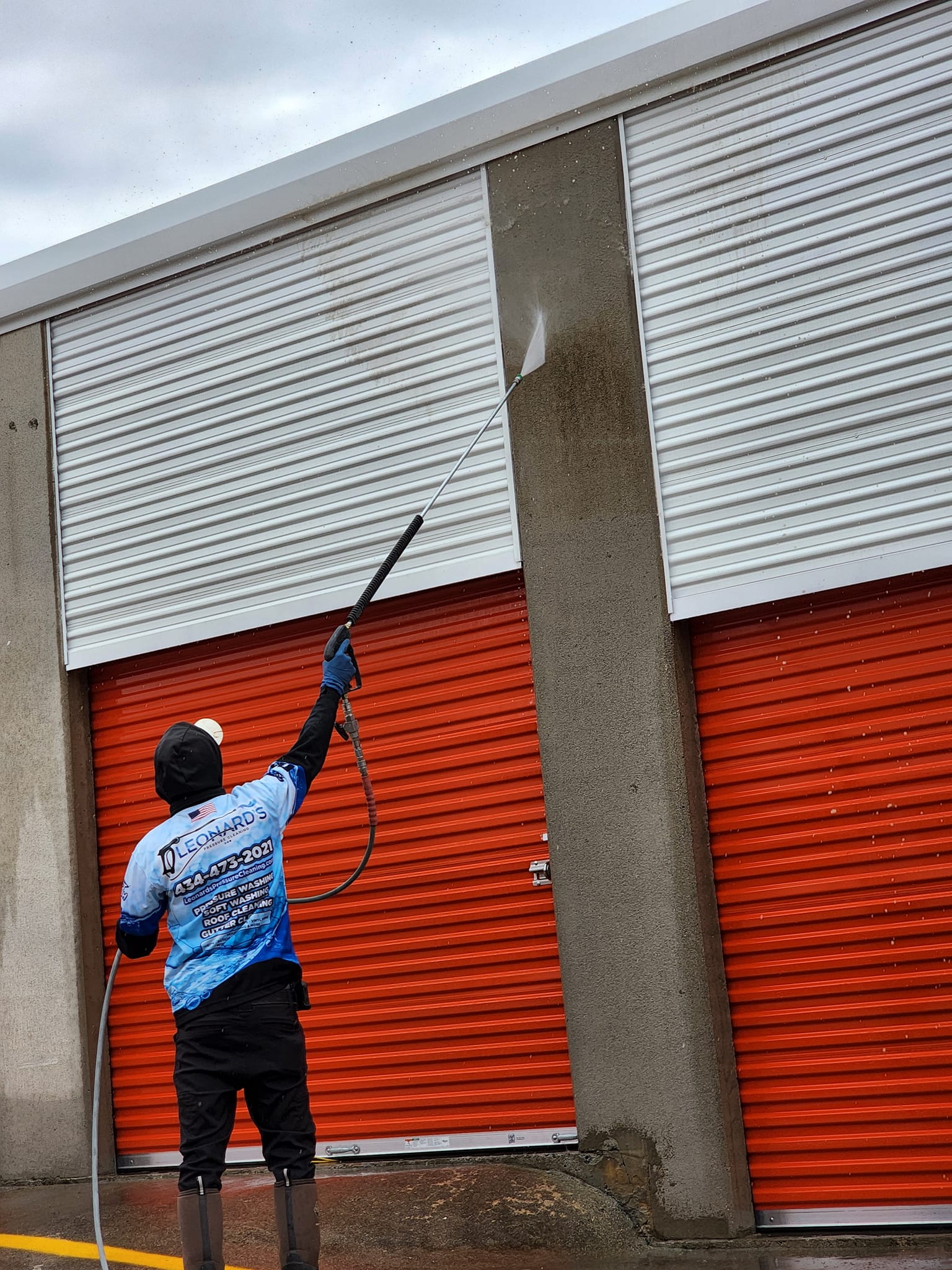 Person pressure washing a concrete pillar, with red storage units in the background.