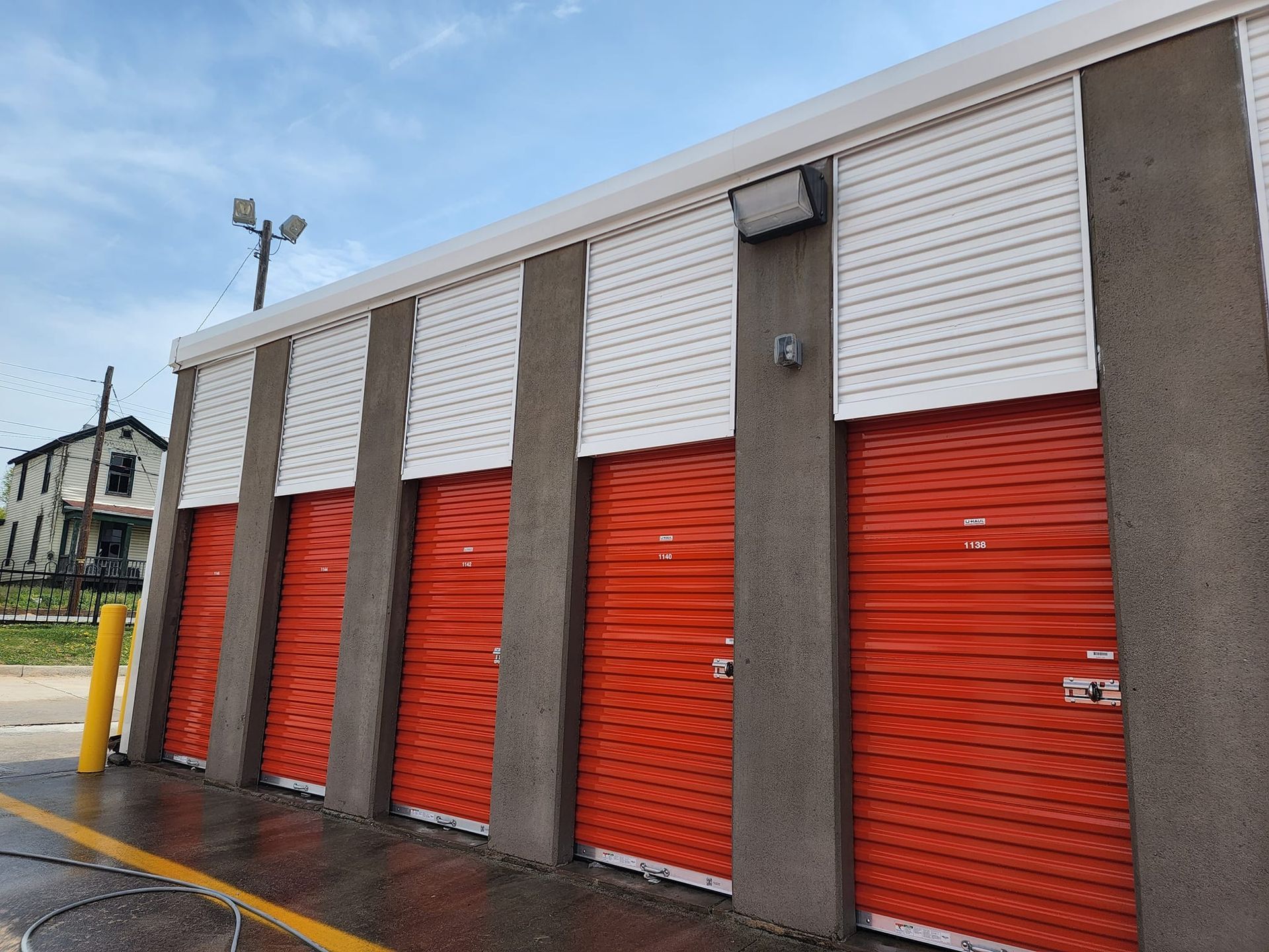 Orange storage unit doors with white overhead, concrete columns, against a cloudy blue sky.