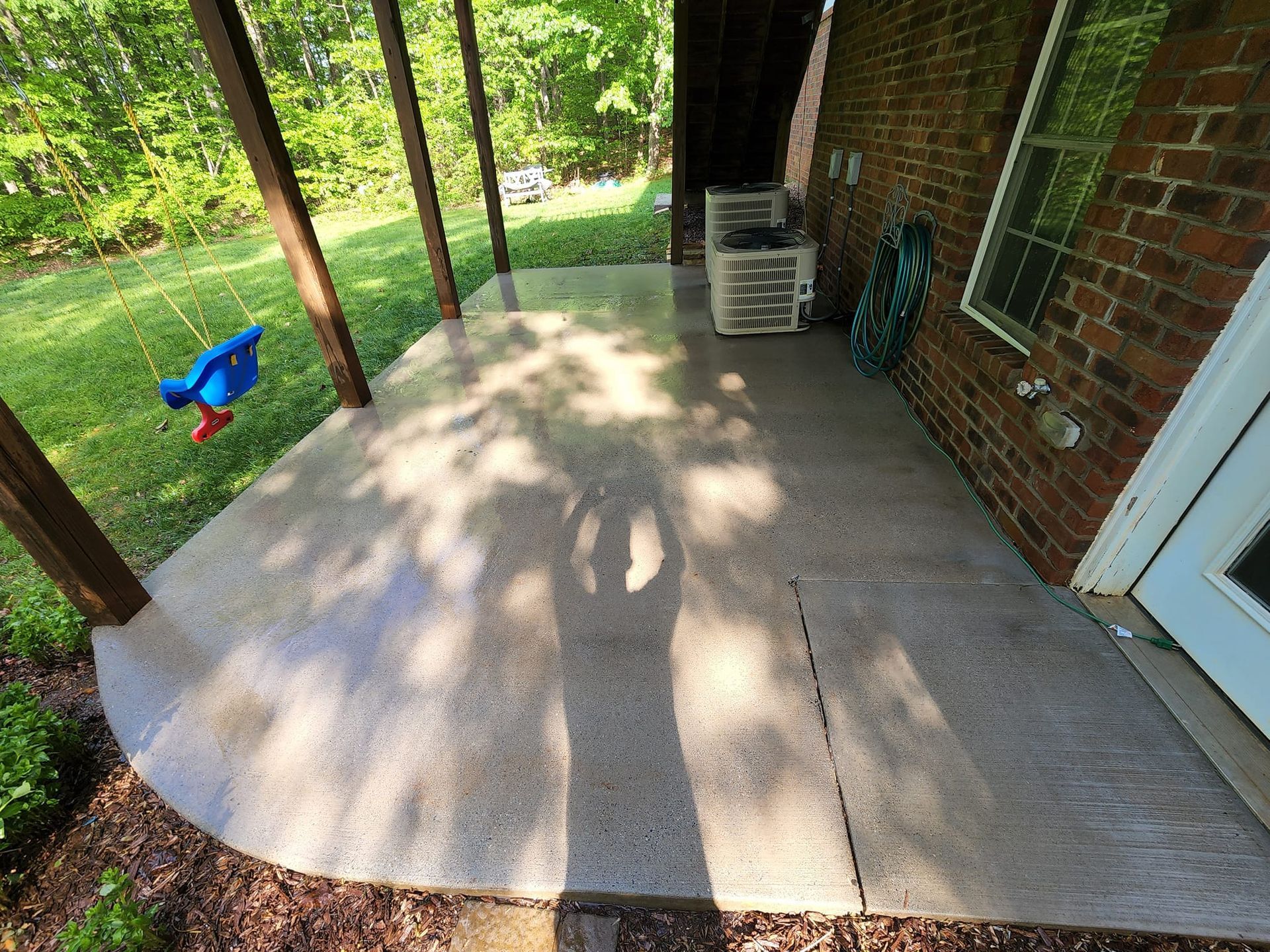 Concrete patio next to a brick house with green lawn and trees in the background.