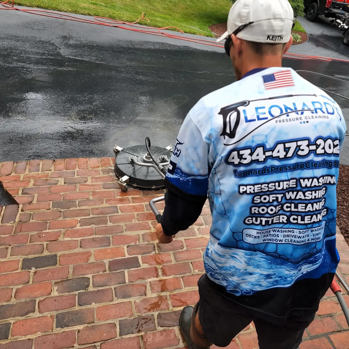 Man pressure washing a brick surface; Leonard Pressure Washing shirt and hat; 434-473-202, outdoors.