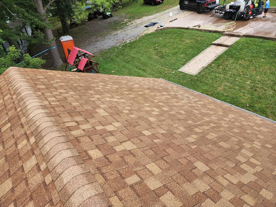 Brown asphalt shingle roof with a lawn and construction vehicles in the background.