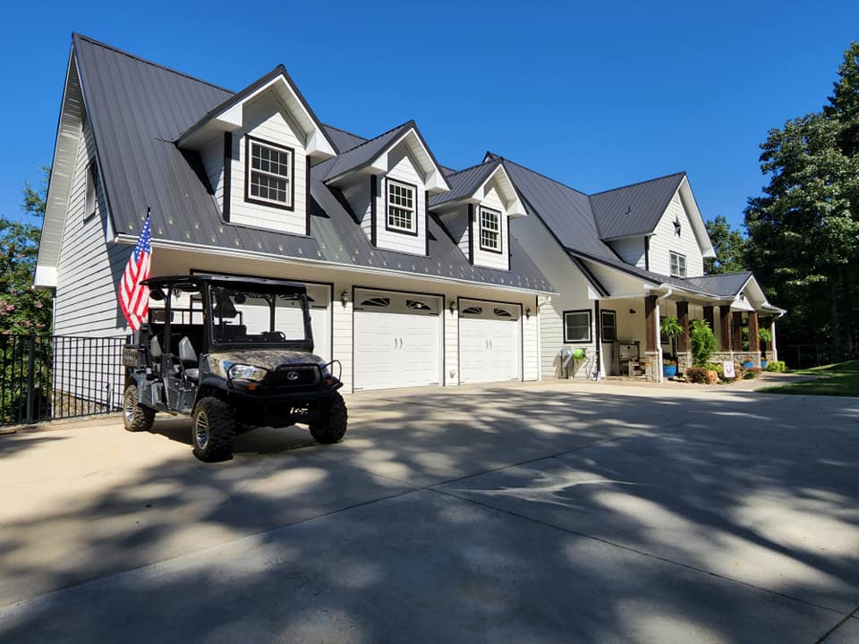 A two-story white house with a black metal roof, three-car garage, and a golf cart on the driveway.