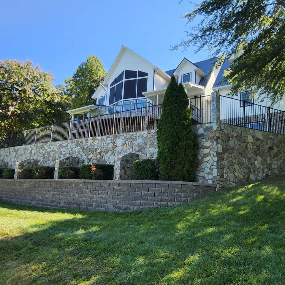 White house with stone retaining walls, green grass, and a clear blue sky.