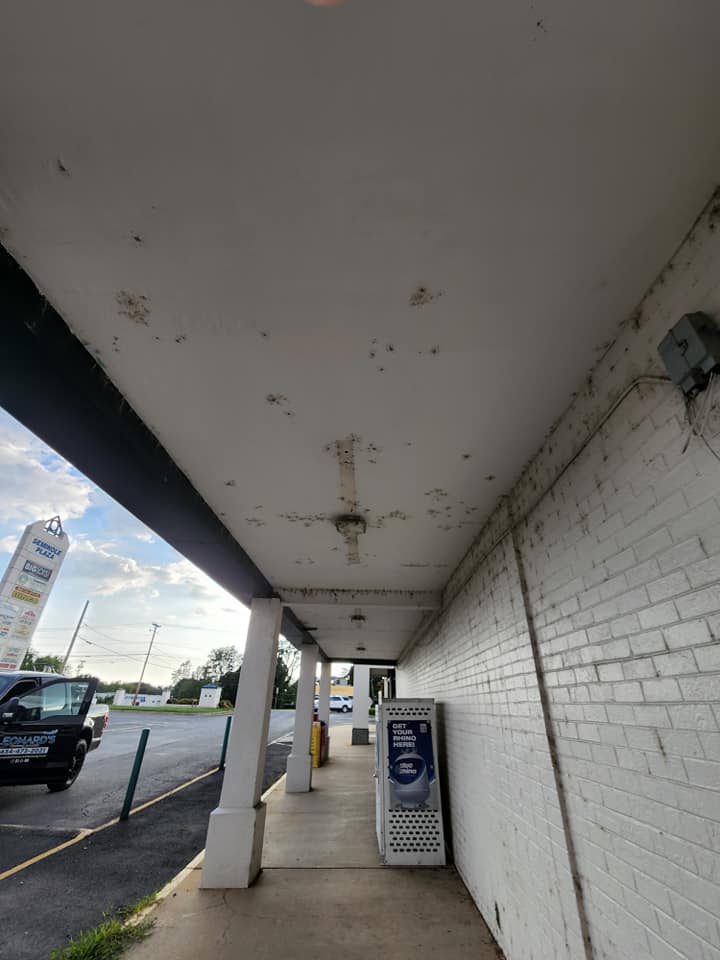Covered walkway with stained ceiling, white brick wall, and a parked vehicle on the left.