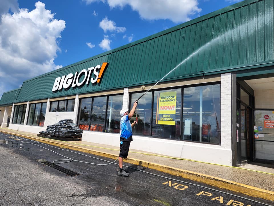 Man pressure washes the exterior of a Big Lots store on a sunny day.