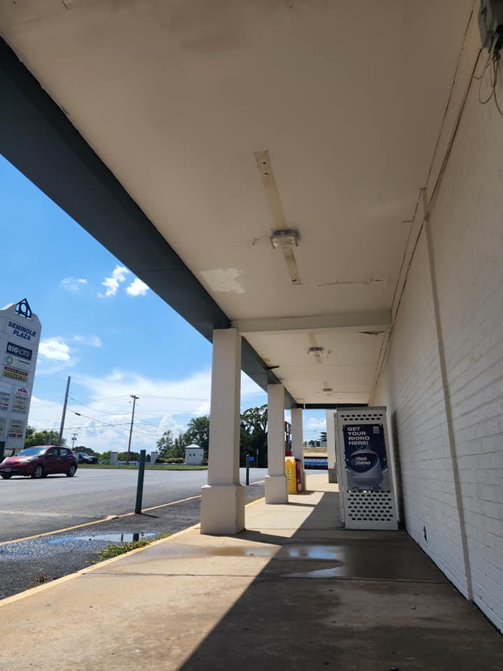 A sidewalk under a white canopy with columns. Cars and a sign in the background on a sunny day.
