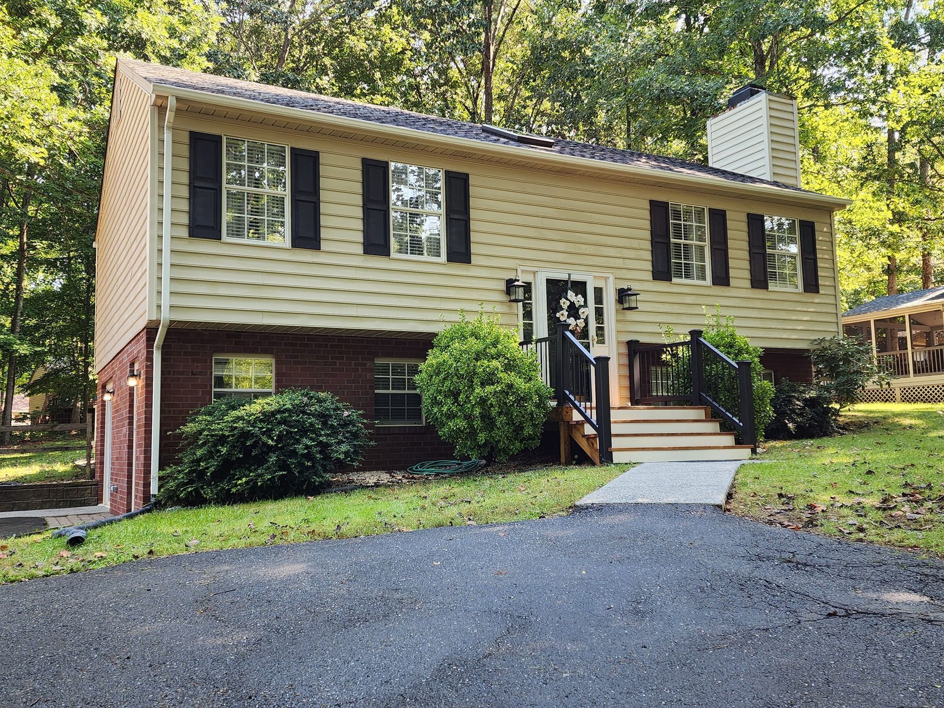 Two-story house with brick lower level, tan siding, black shutters, and a dark driveway.