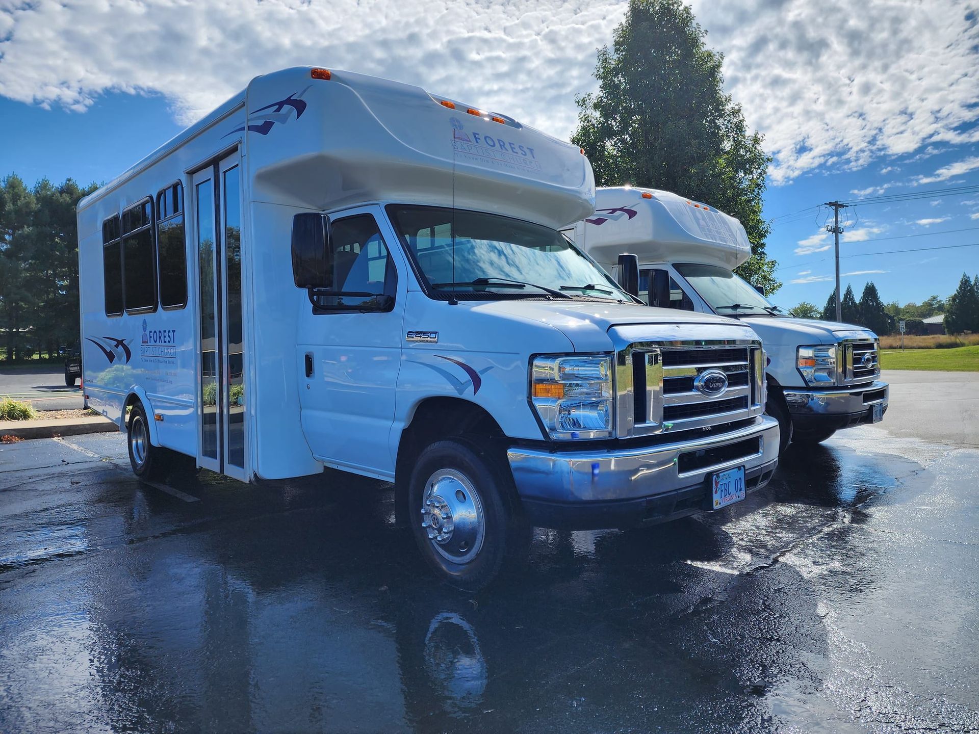 Two white passenger vans parked on a wet surface under a cloudy sky.
