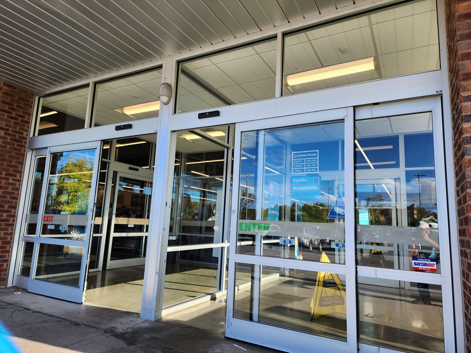 Exterior of a store with glass automatic sliding doors. Sunlight, building with brick and windows.