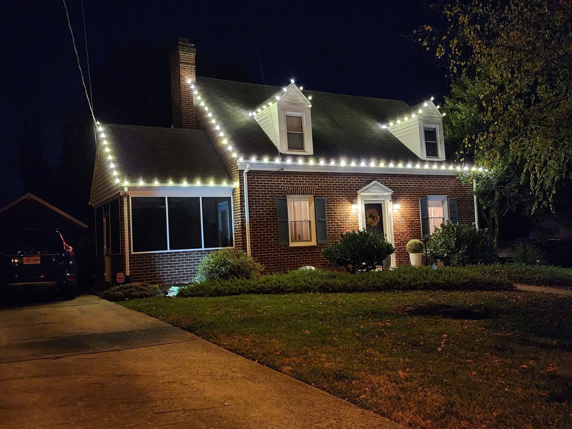 Brick house at night with white lights outlining the roof, front porch, and dormers.