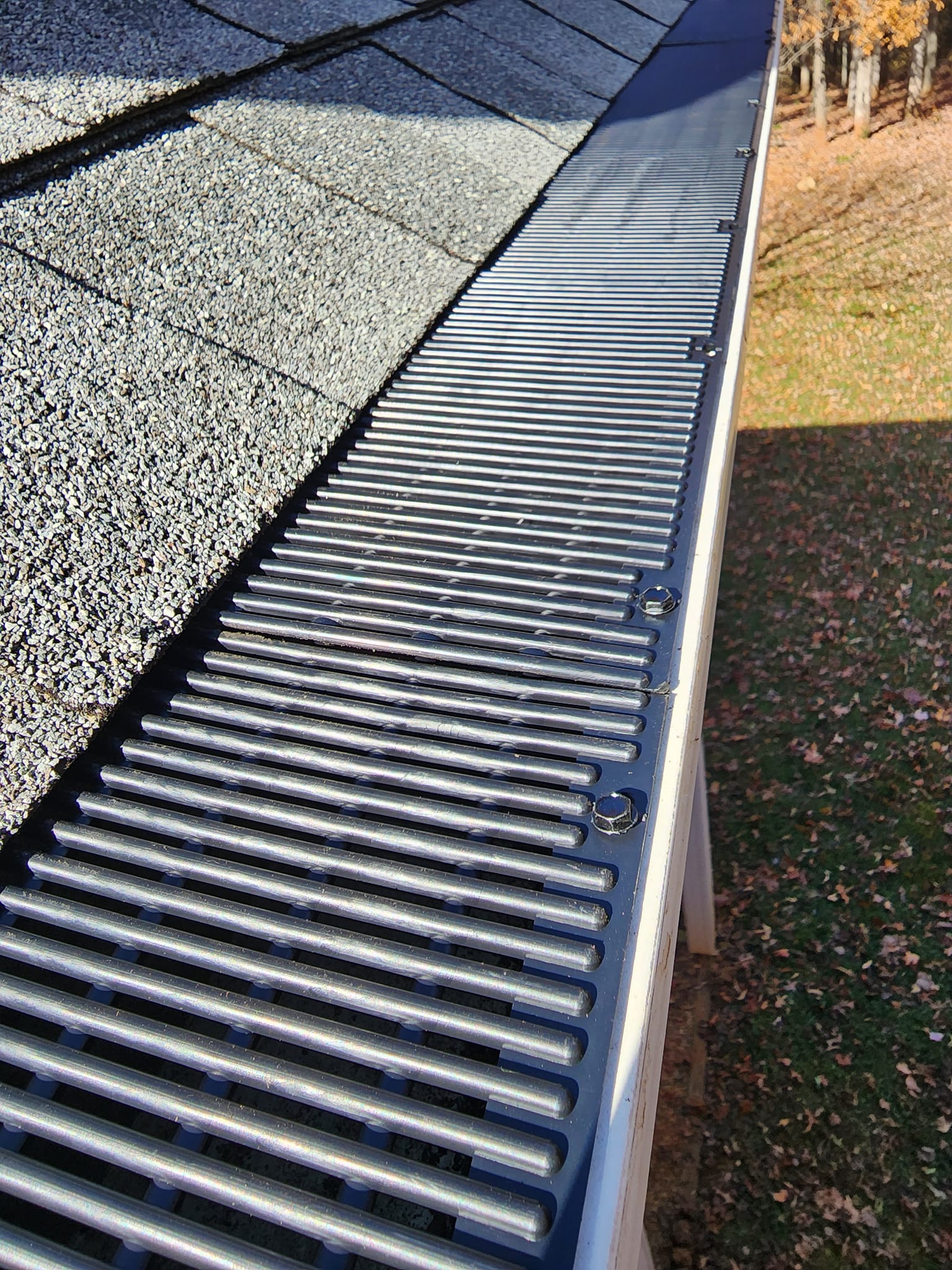 Gutter guard installed on a roof. Close-up view shows the guard's horizontal bars, alongside dark shingles and the roof's edge.