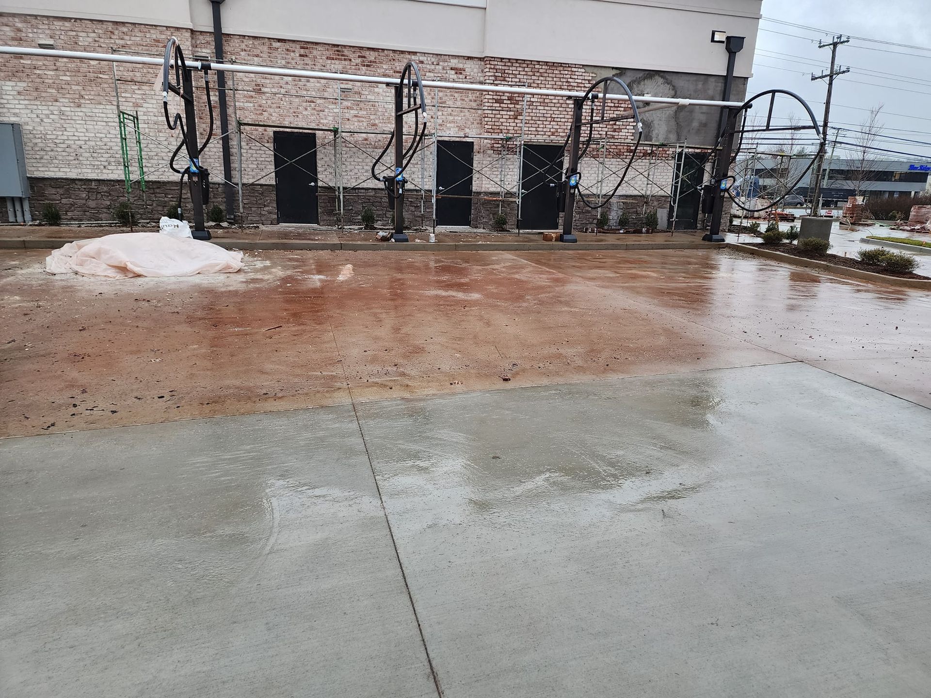 A wet car wash bay with water on the concrete floor; equipment, doors, and a foamy area are visible.