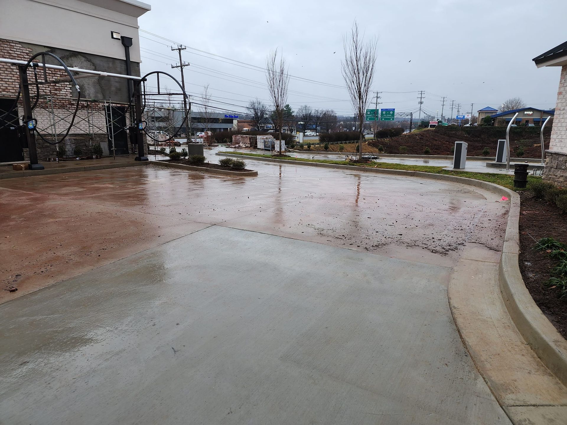 Wet concrete at a car wash entrance on a rainy day, with a view of city in the distance.