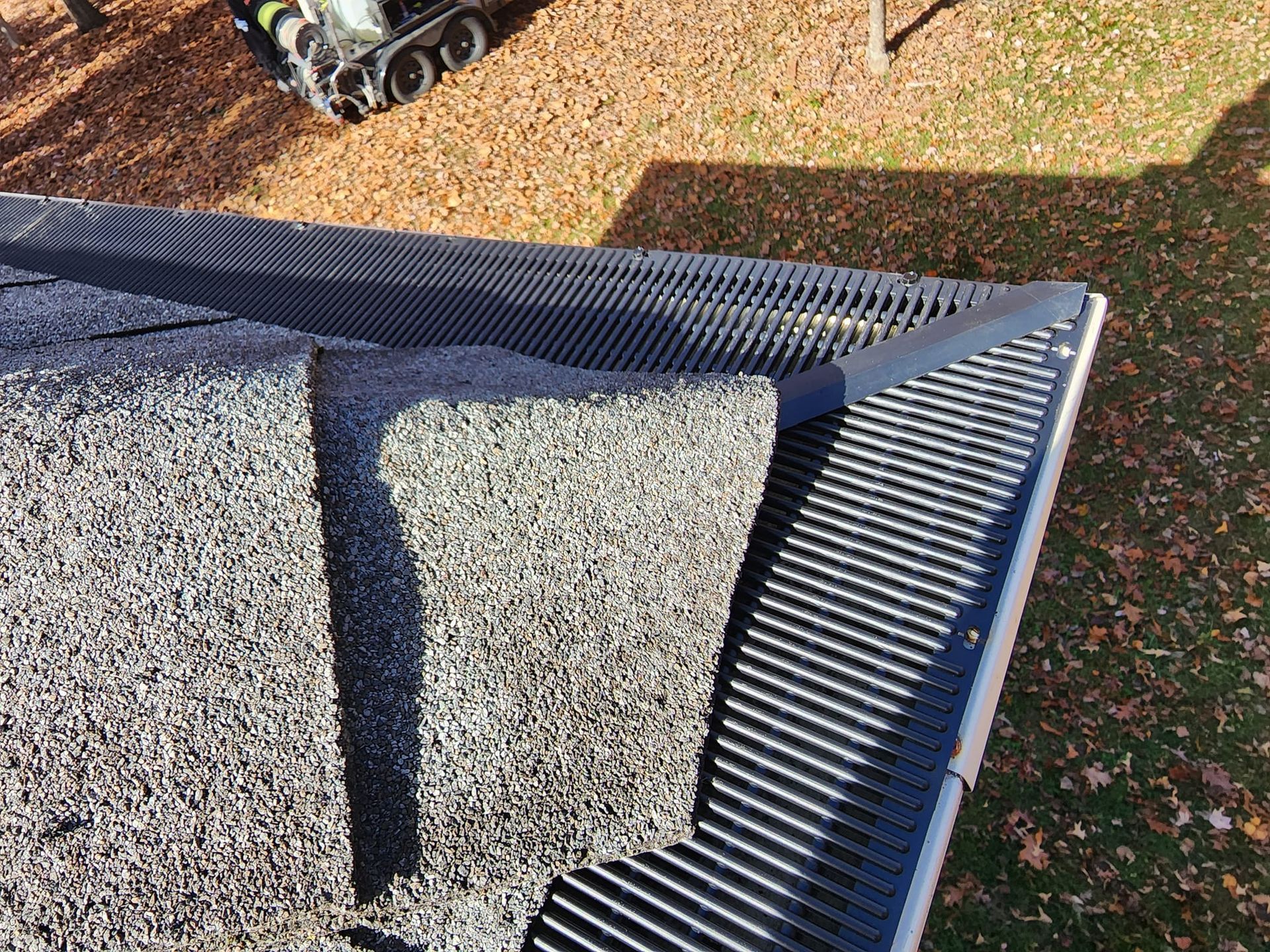 Close-up of a thatched roof corner; black trim, gray thatch, and a glimpse of fall leaves.