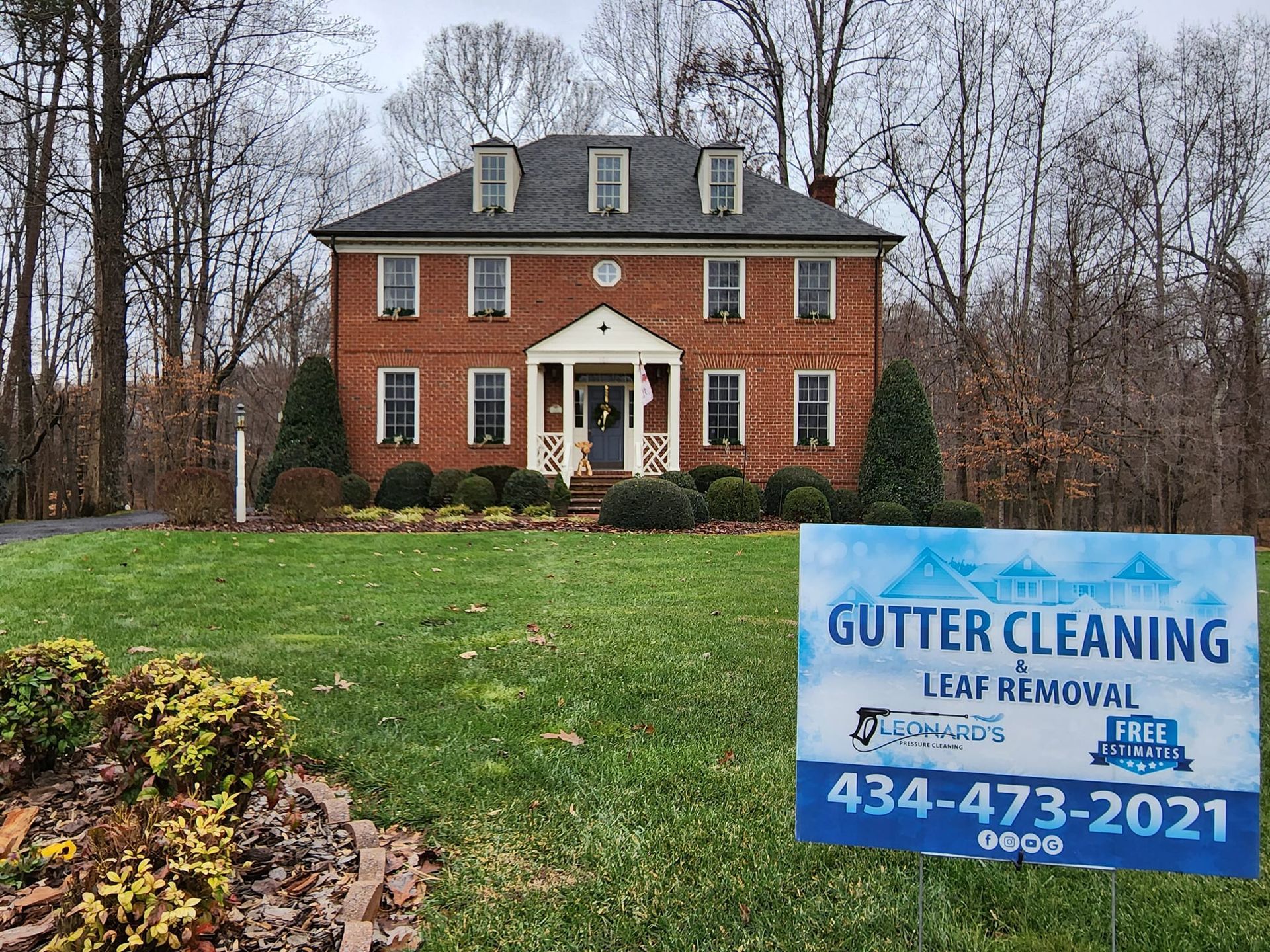 Two-story brick house with gutter cleaning sign on lawn; contact info 434-473-2021.