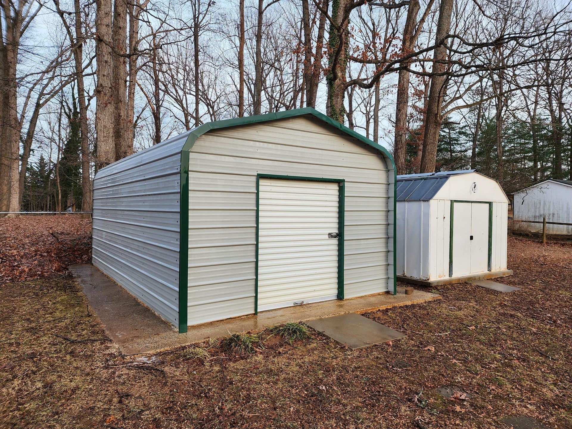 Two metal sheds with green trim, one larger and one smaller, outdoors in a yard.