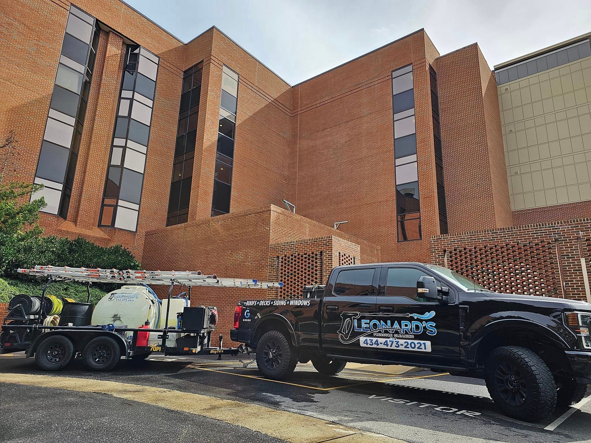 Black truck with trailer parked in front of a brick building, advertising Leonard's services.