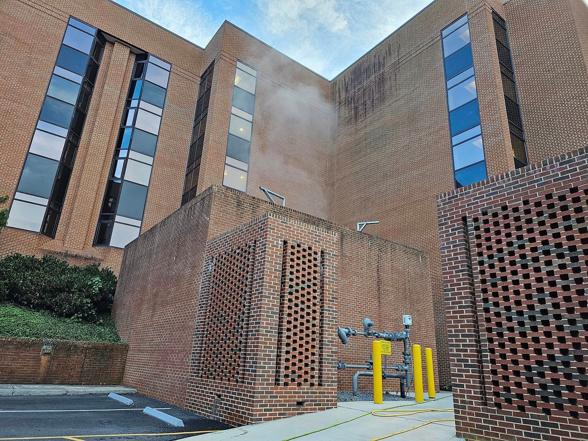 Brick building with rectangular windows, brick enclosure with yellow pipes. Cloudy sky.
