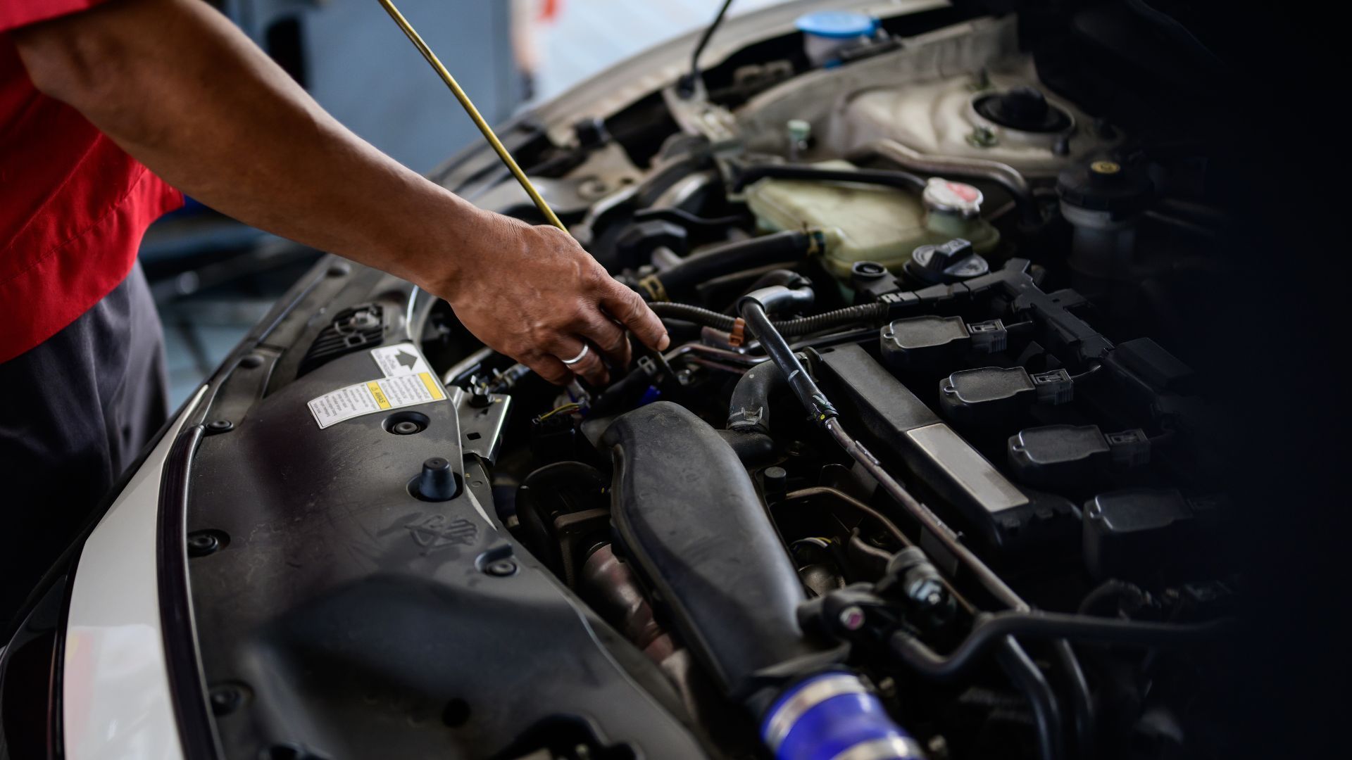 Mechanic working on a car engine in a garage; checking oil with dipstick.