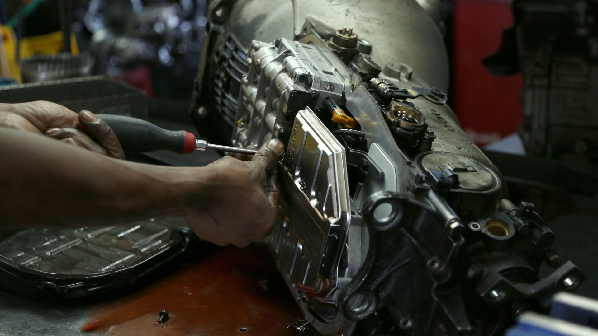 Mechanic using a screwdriver to work on a car transmission.