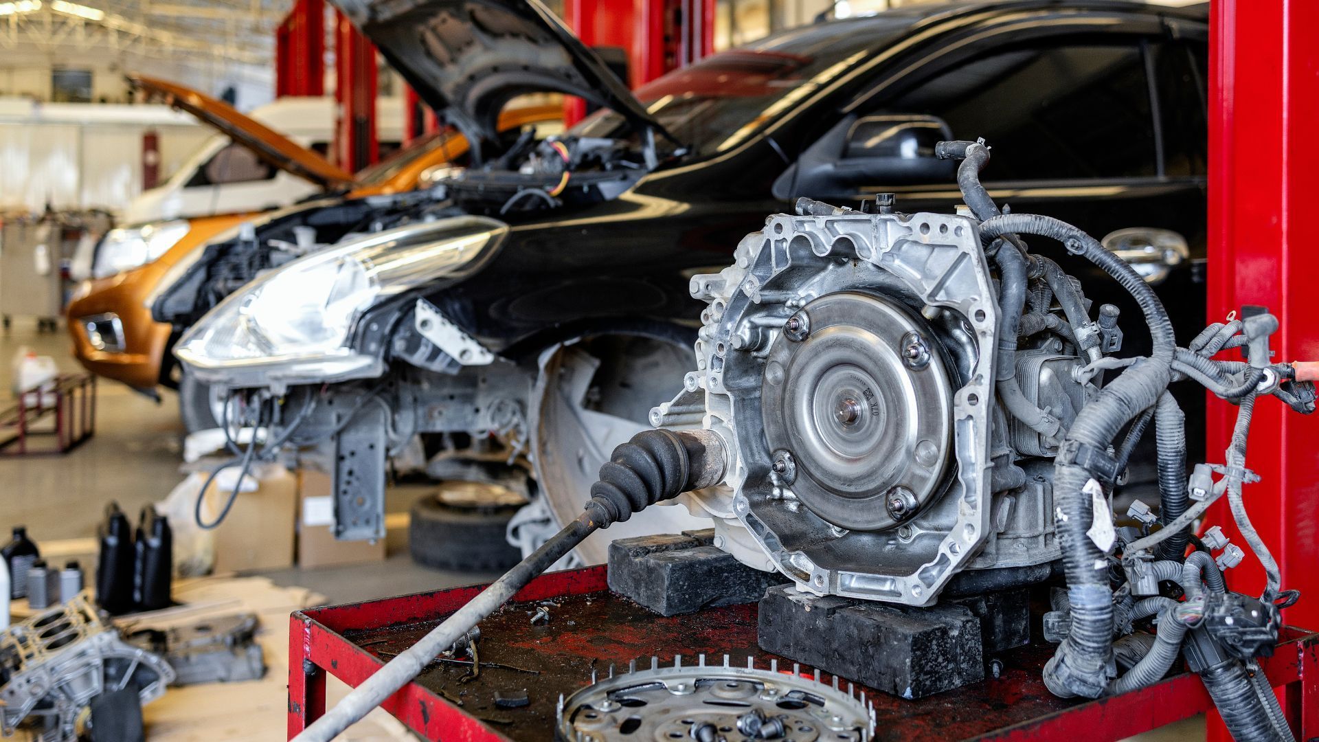 Car engine and parts on a workbench in an auto repair shop with two cars being worked on.