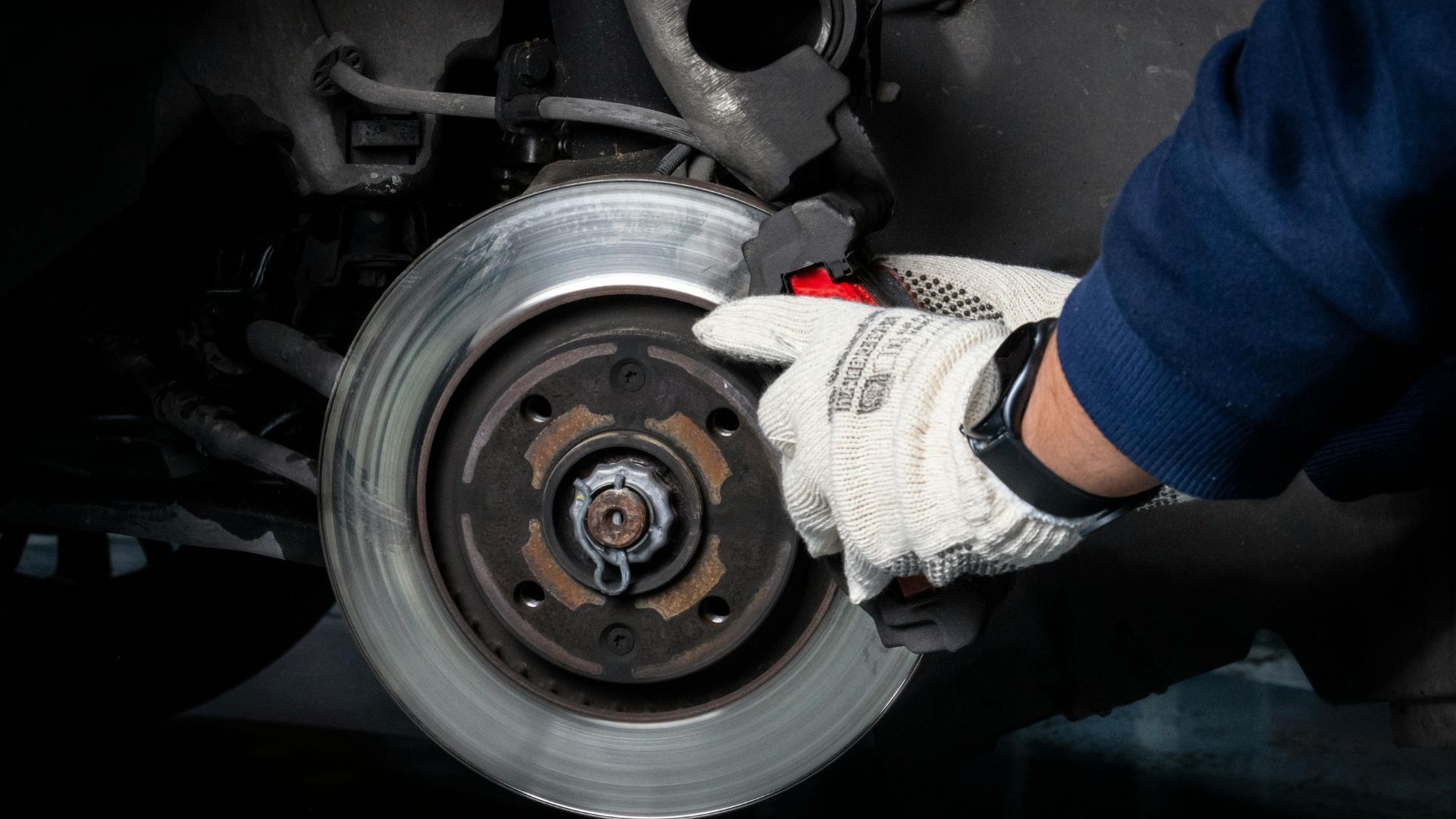 Mechanic's gloved hand working on a car brake rotor, inspecting the pads.