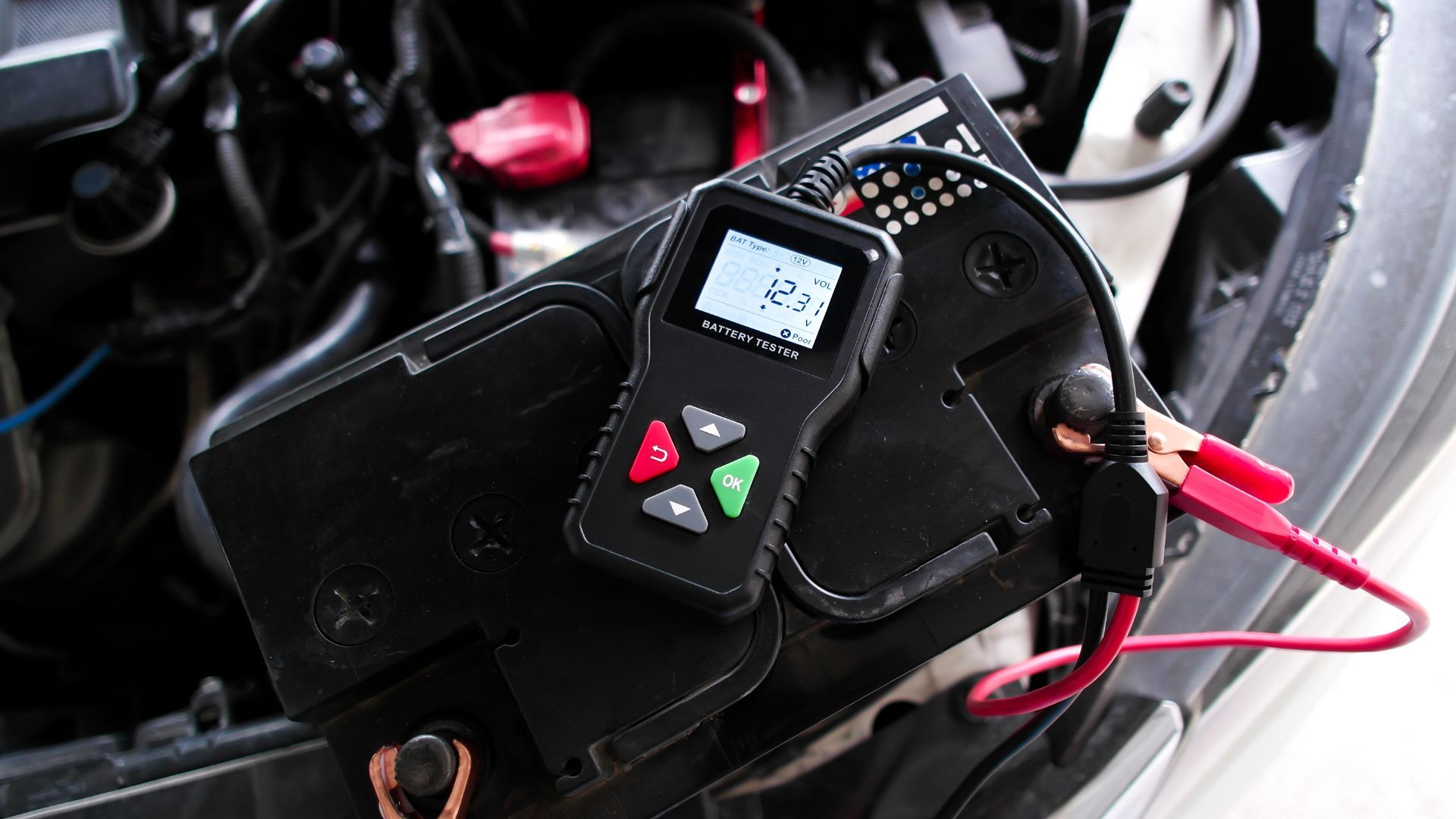 Battery tester connected to a car battery; shows 12.7 volts.