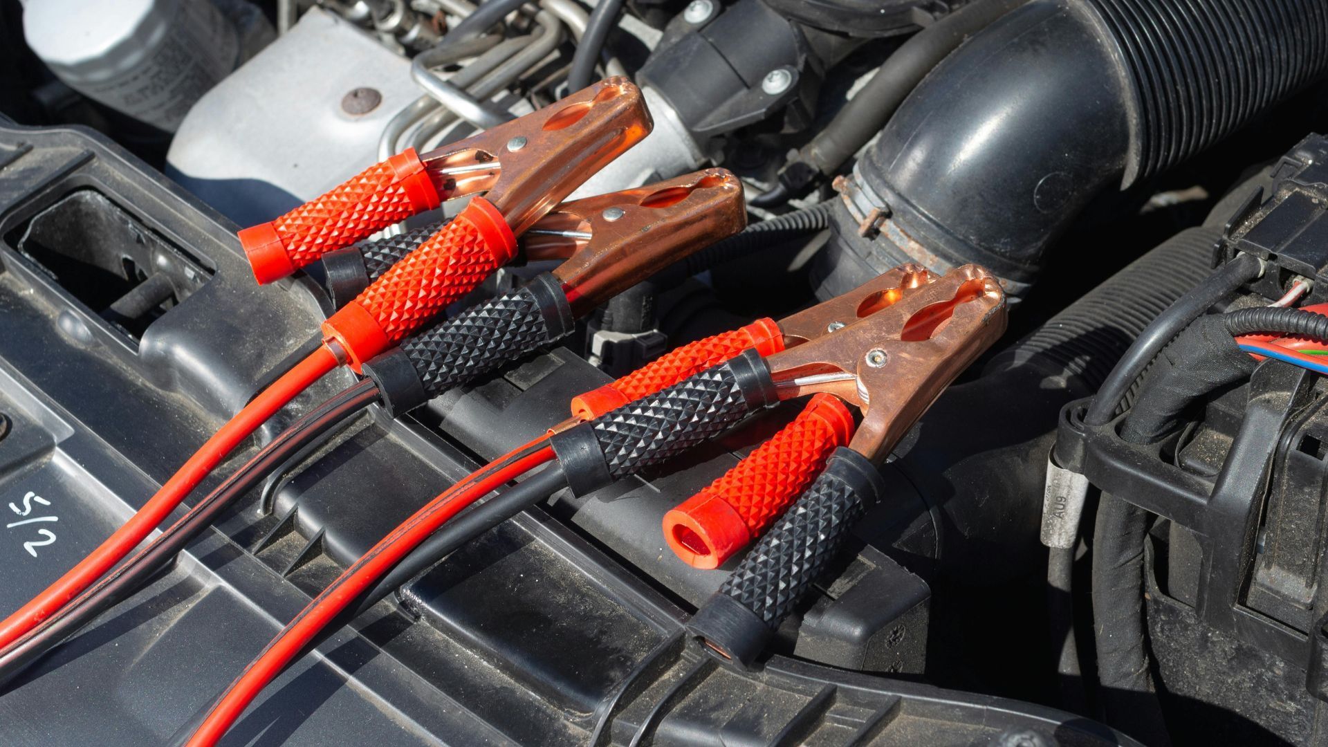 Jumper cables connected to car battery, red and black cables with clamps in engine bay.