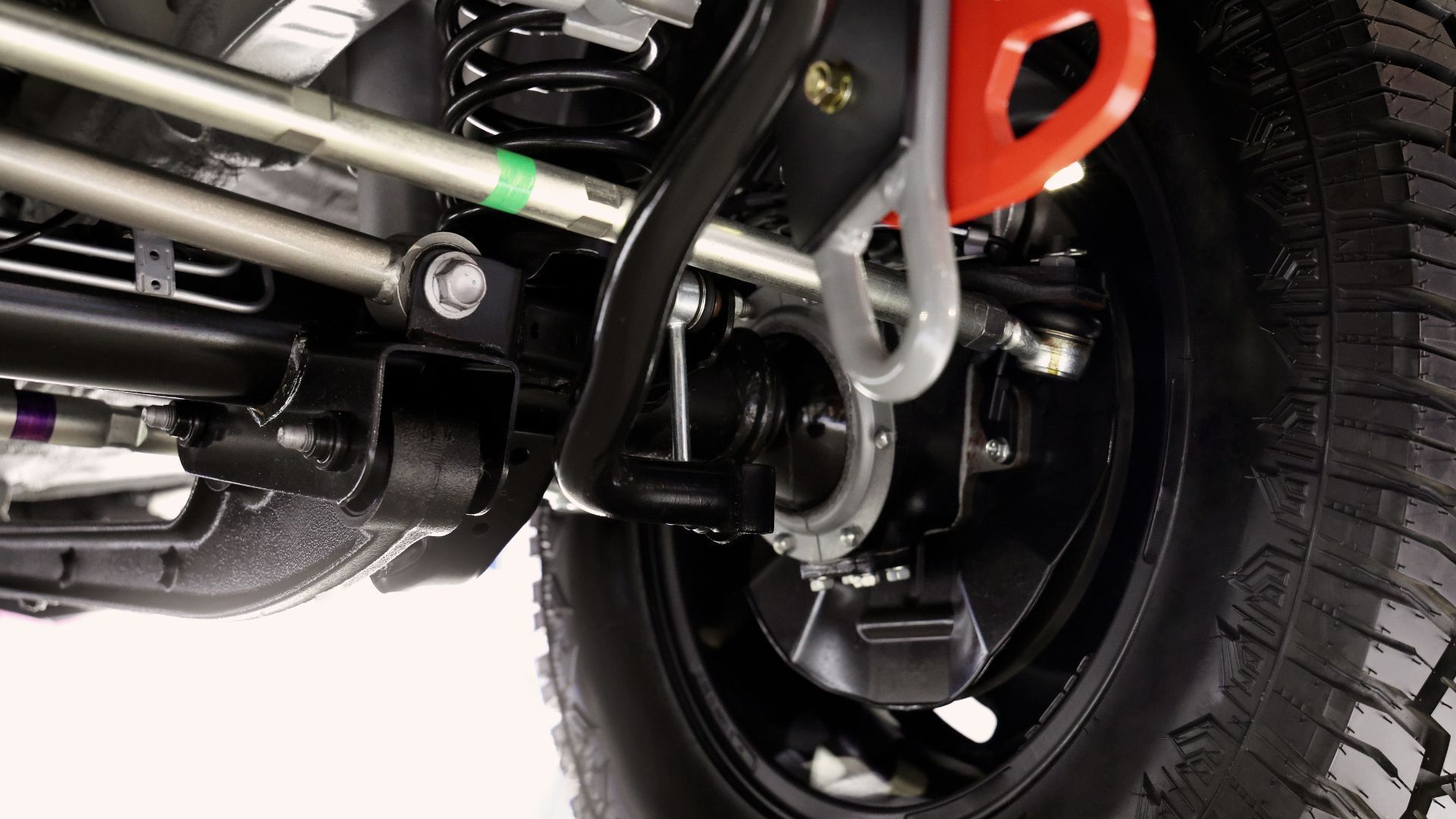 Close-up of a black vehicle's rear suspension, with tire. Orange recovery hook visible.