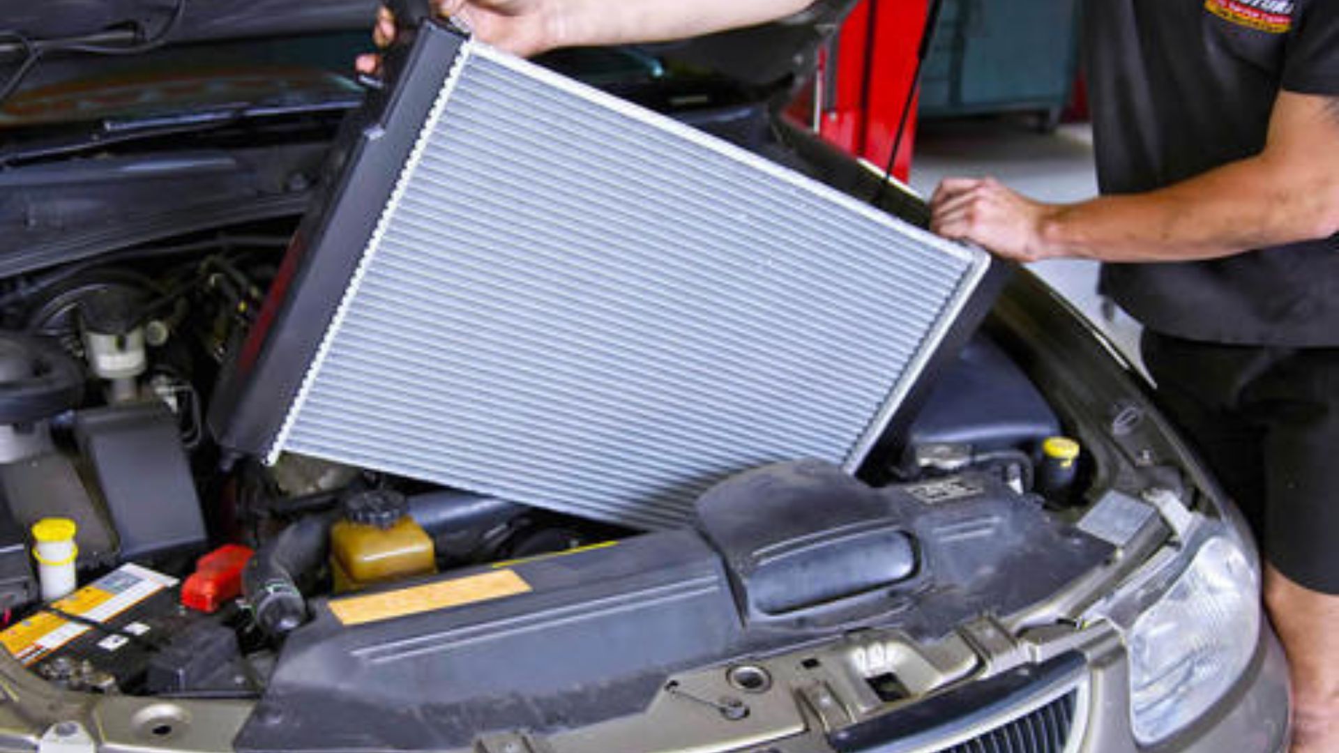 Mechanic removing a radiator from a car engine.