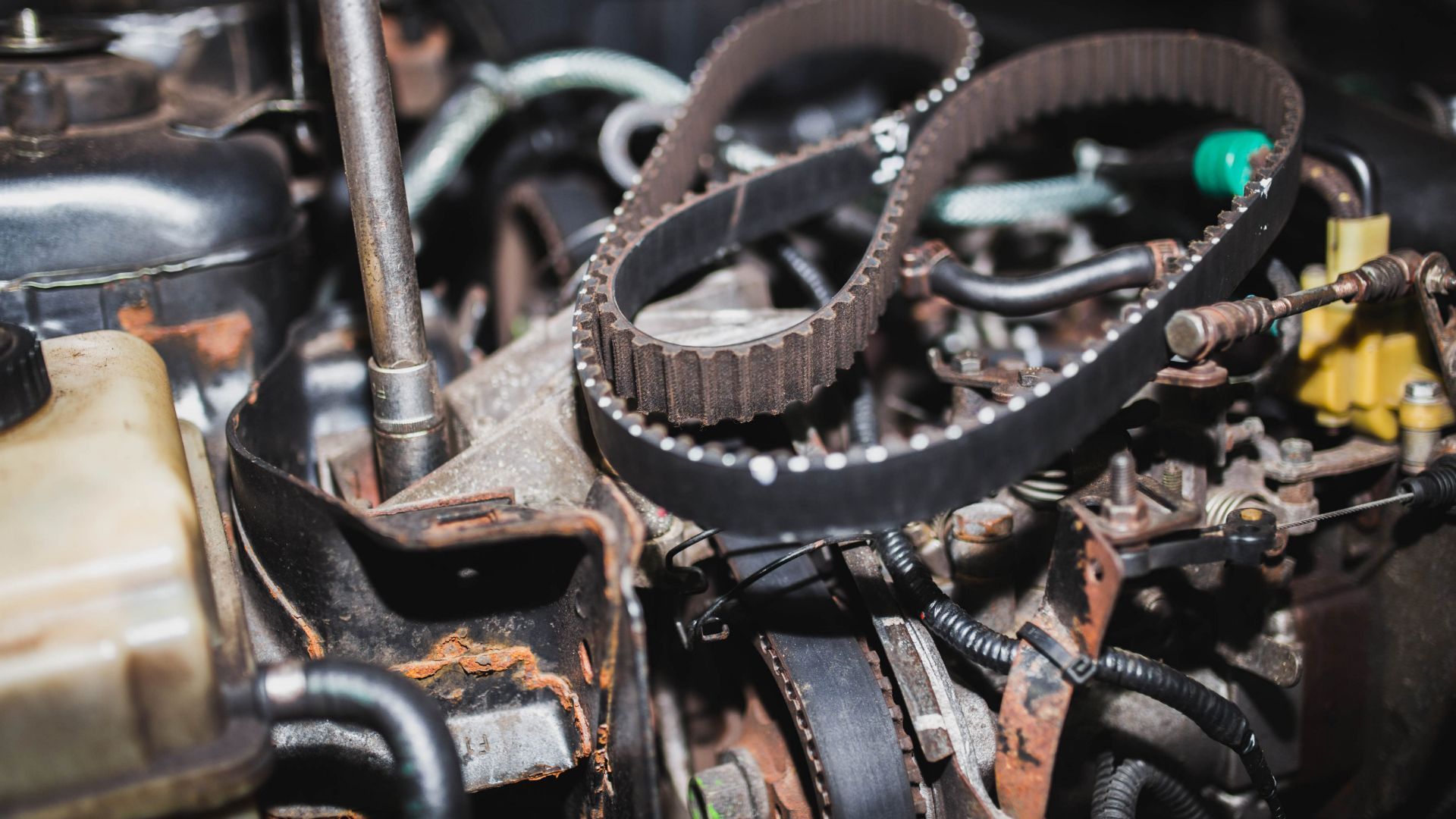 Close-up of a timing belt in a car engine, highlighting its toothed structure amidst other engine components.
