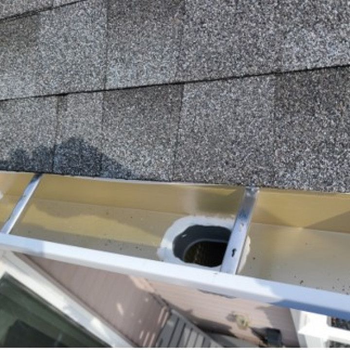 Gutter with a downspout opening beneath gray asphalt shingles; a light-colored gutter is visible.