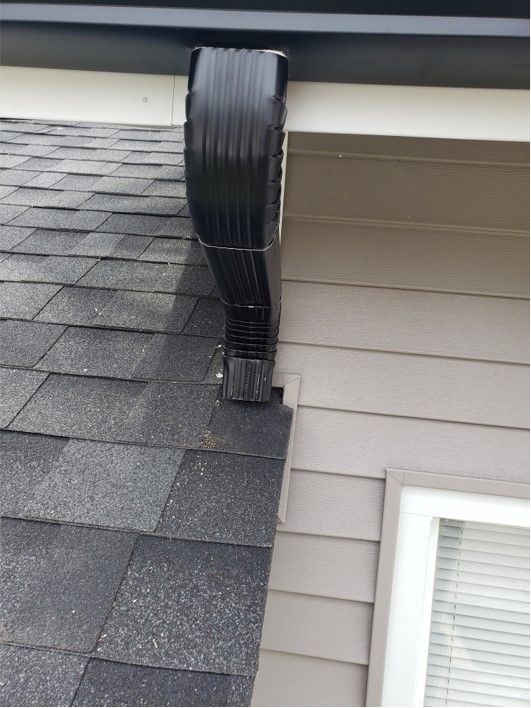 Black gutter pipe attached to a roof and beige wall, directing water down.