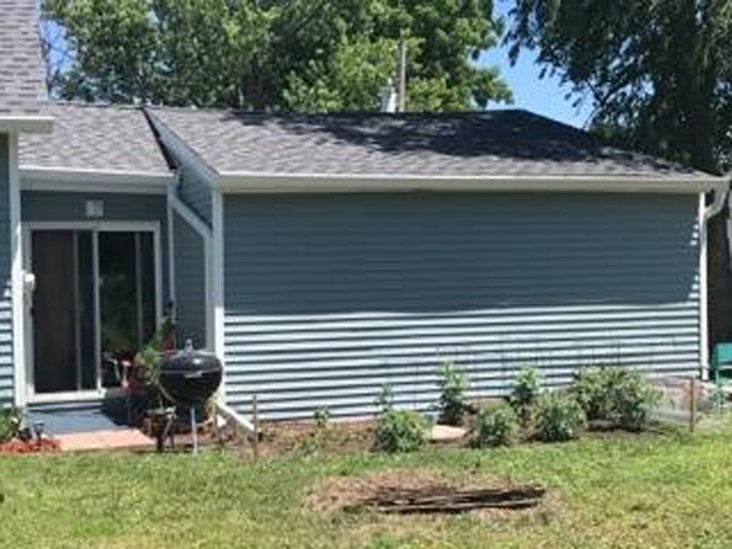 Blue house with a sliding door, grill, and garden in a yard.