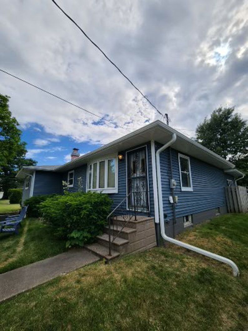 Blue house with white trim and a dark screen door, small concrete steps, and green lawn.