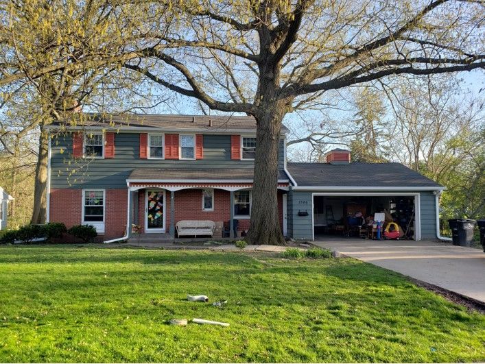 Two-story house with teal siding, red brick, and a large tree in front. Garage on the right.