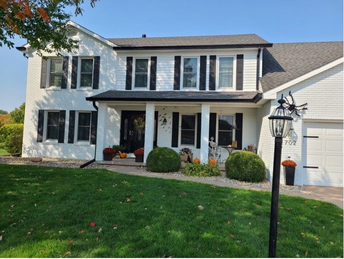White house with black shutters, front porch, and green lawn. Pumpkins and autumn decor.