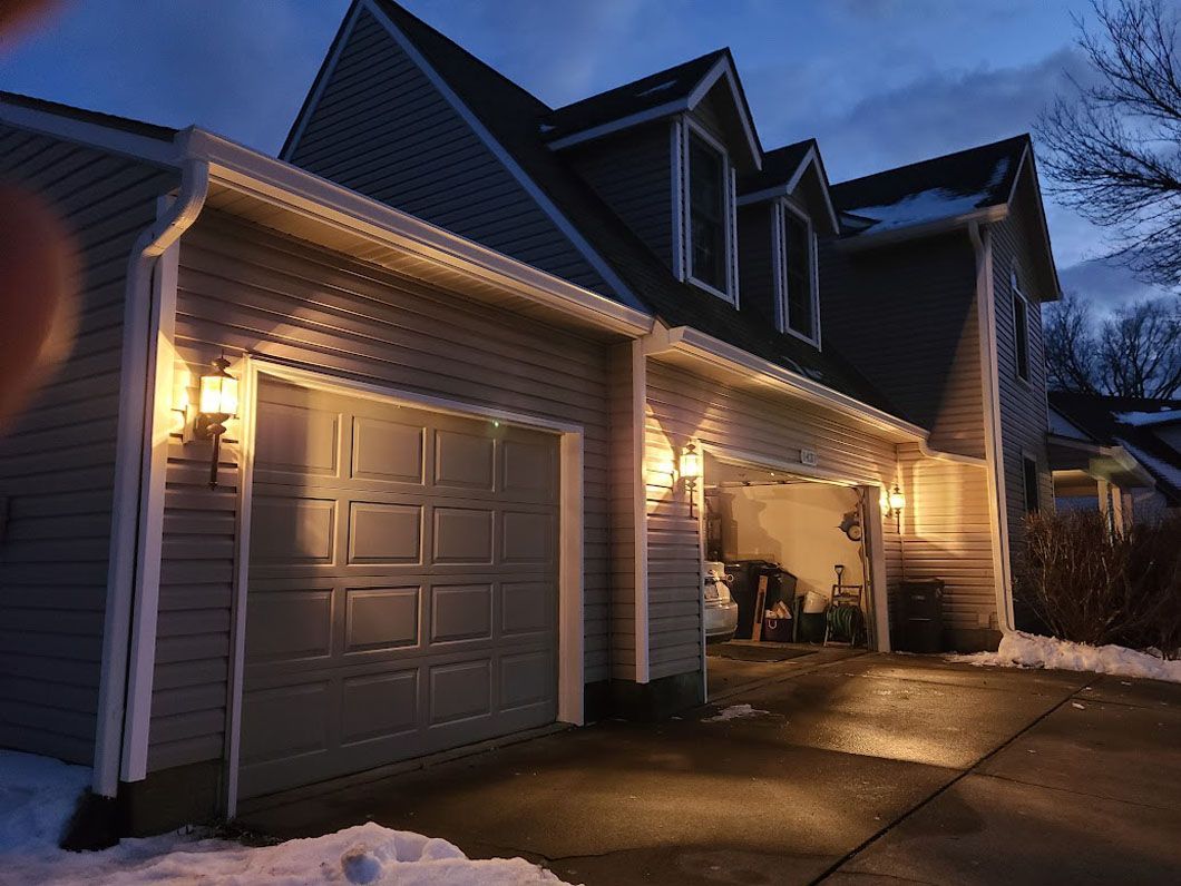 Two-story house at dusk with lit garage. Garage door closed, car in open bay. Snow on the ground.
