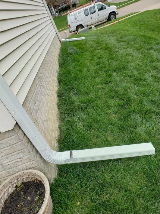 Gray guttering along beige house, emptying onto green lawn. A white van sits in the background.